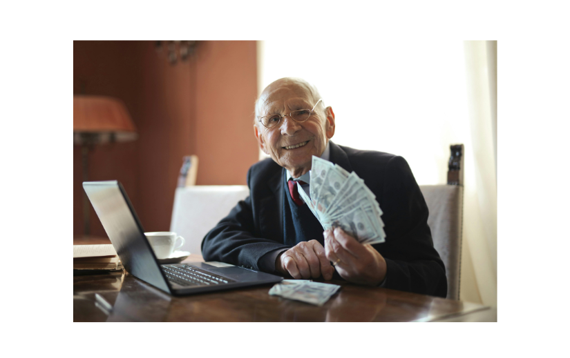 Elderly businessman demonstrating eCommerce growth, smiling with cash in hand at his laptop.